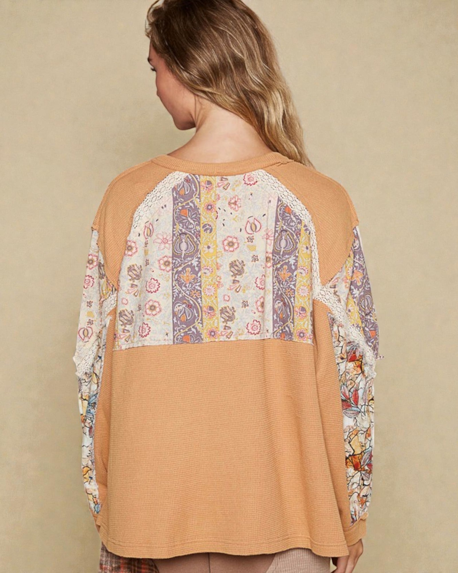 Woman wearing a tan top with floral lace sleeves and back panel on a beige background