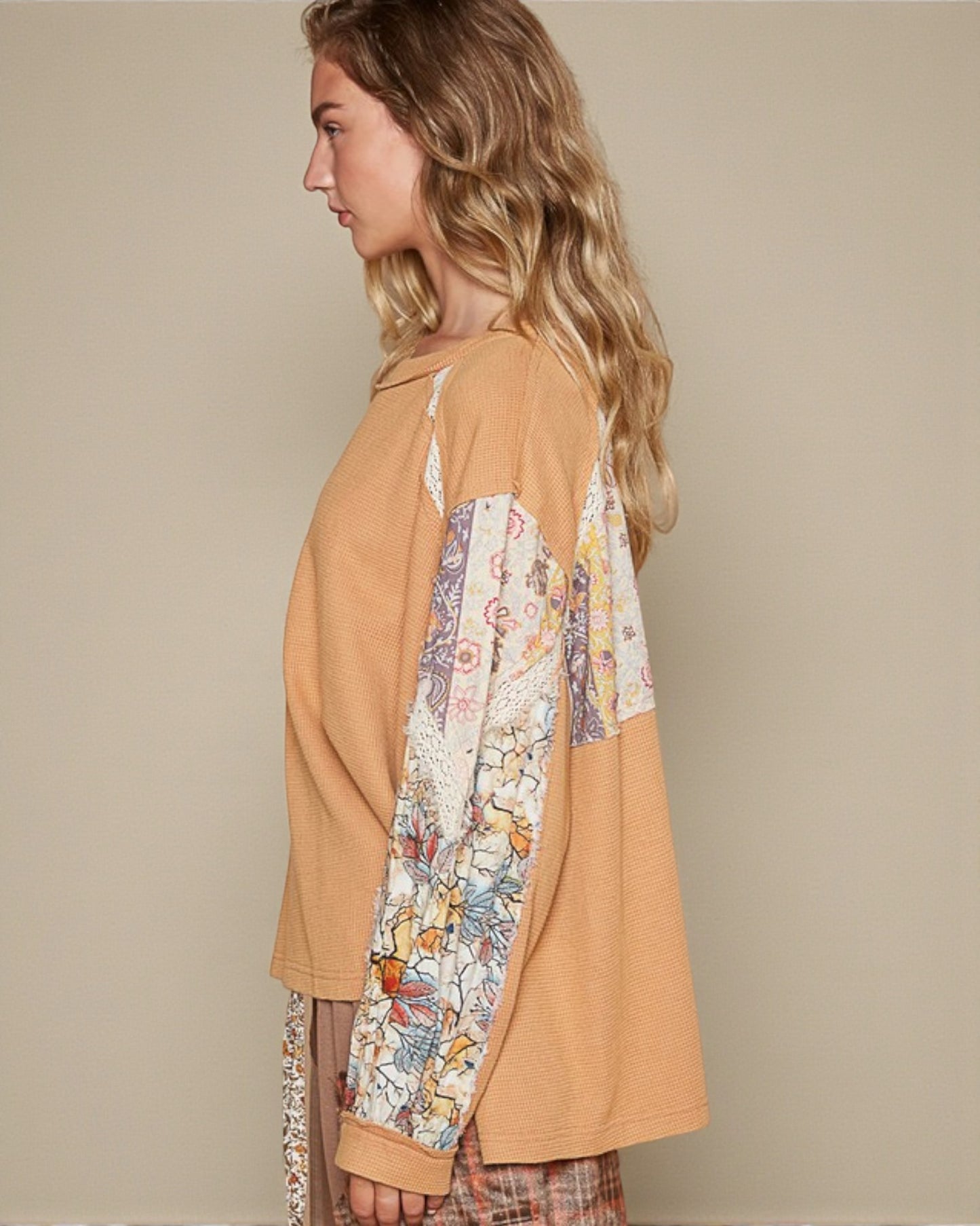 Woman wearing a mustard yellow top with floral sleeves against a beige background