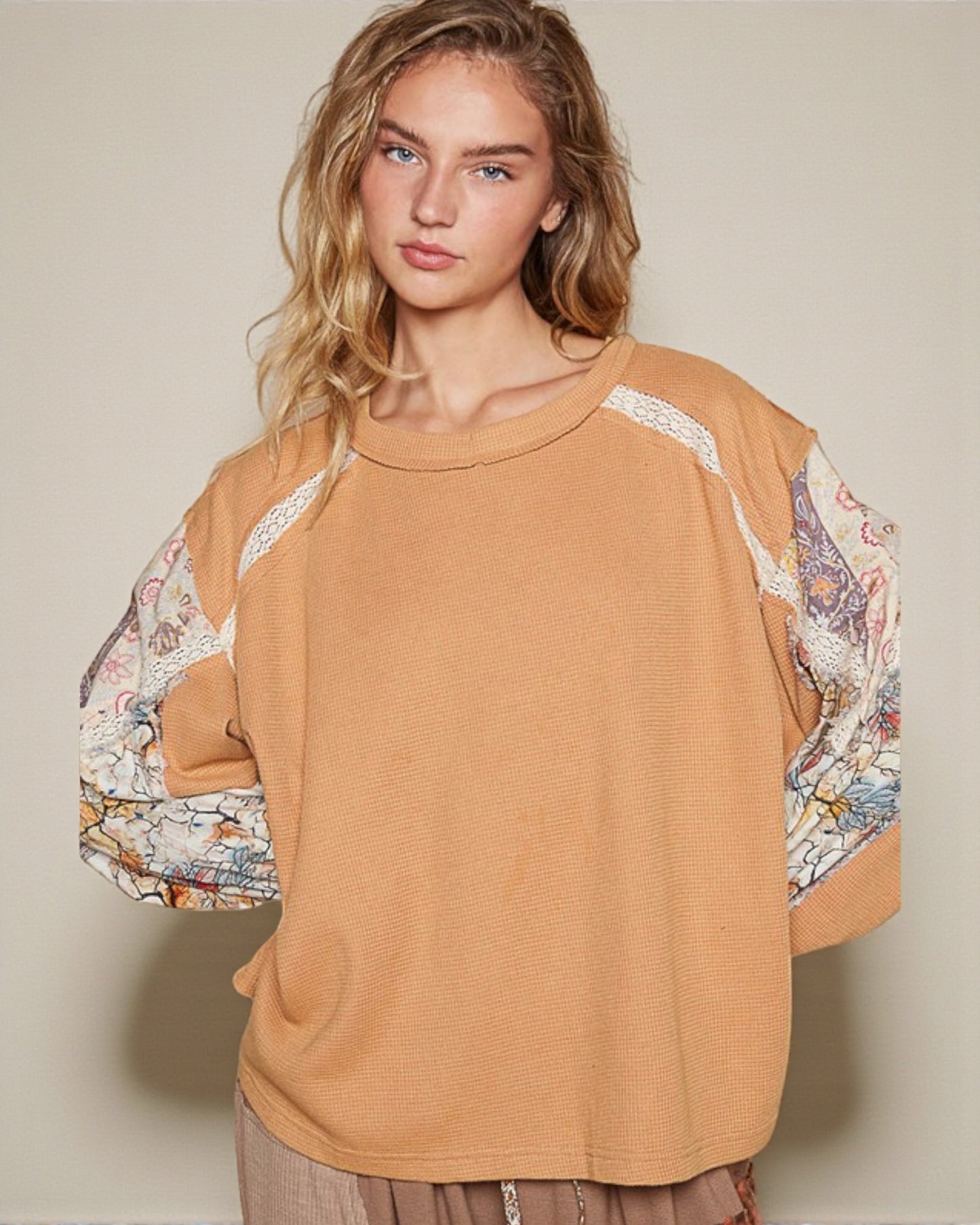 Woman wearing a mustard yellow sweater with floral sleeves against a beige background
