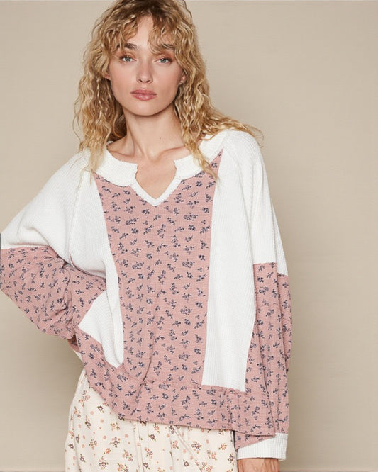 Woman wearing a pink floral blouse with a white cardigan against a beige background