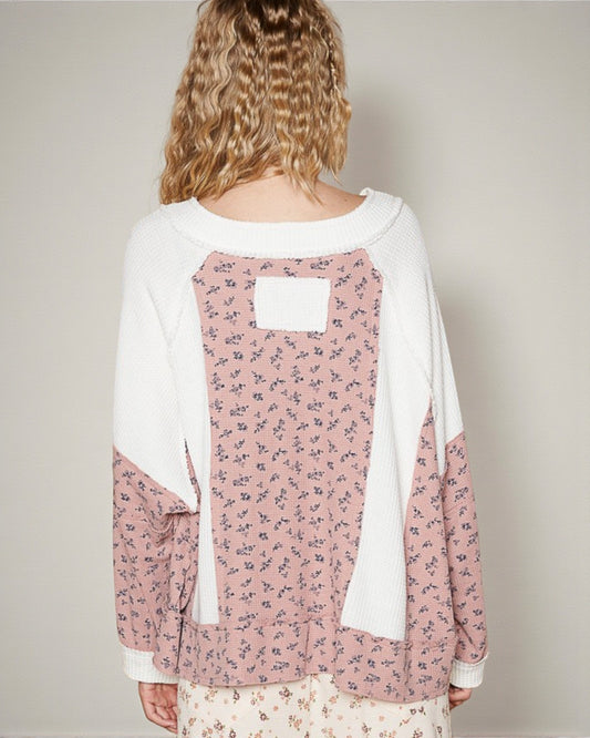 Person wearing a pink floral blouse with a white cardigan on a plain background