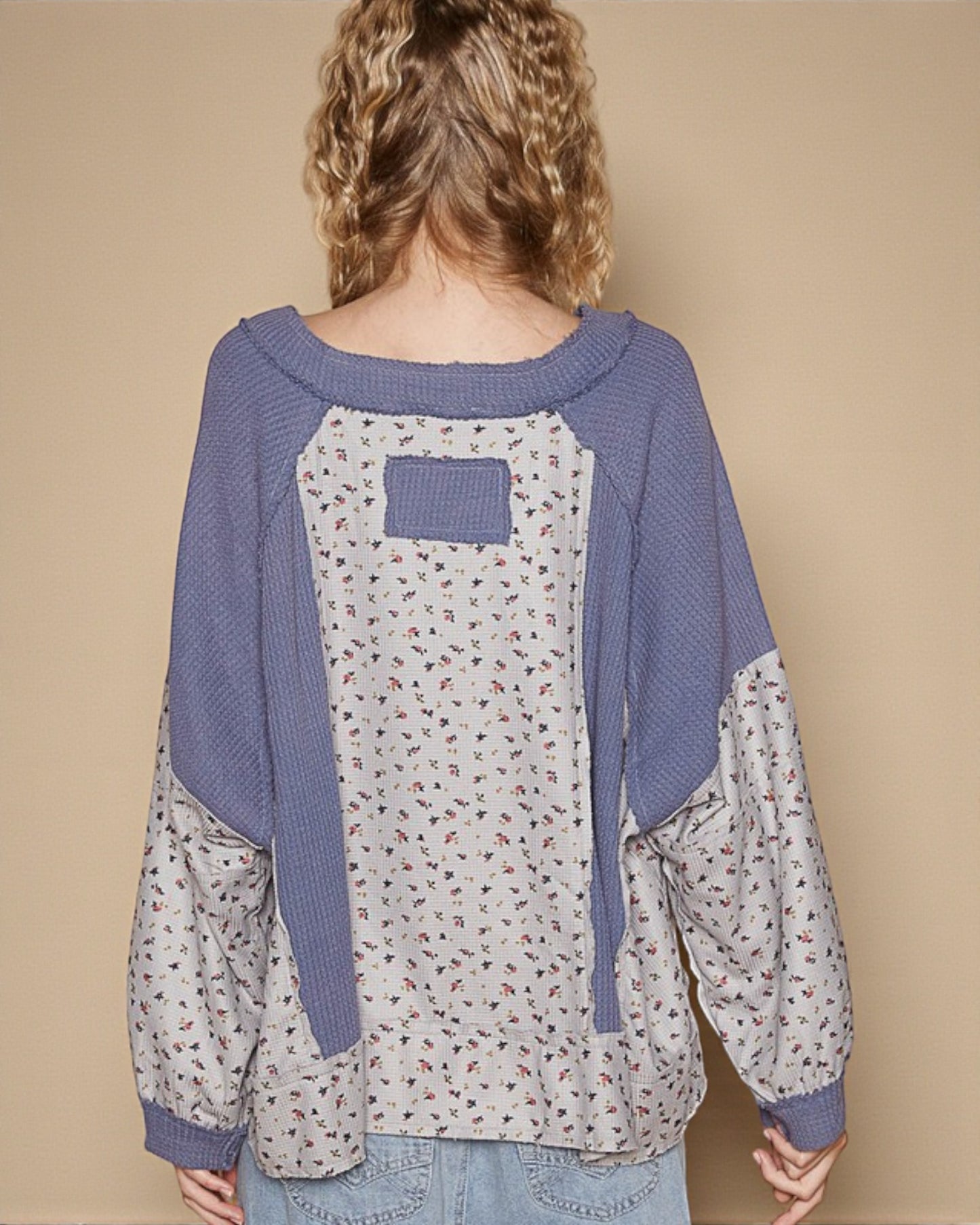 Person wearing a blue and patterned long-sleeve shirt against a beige background