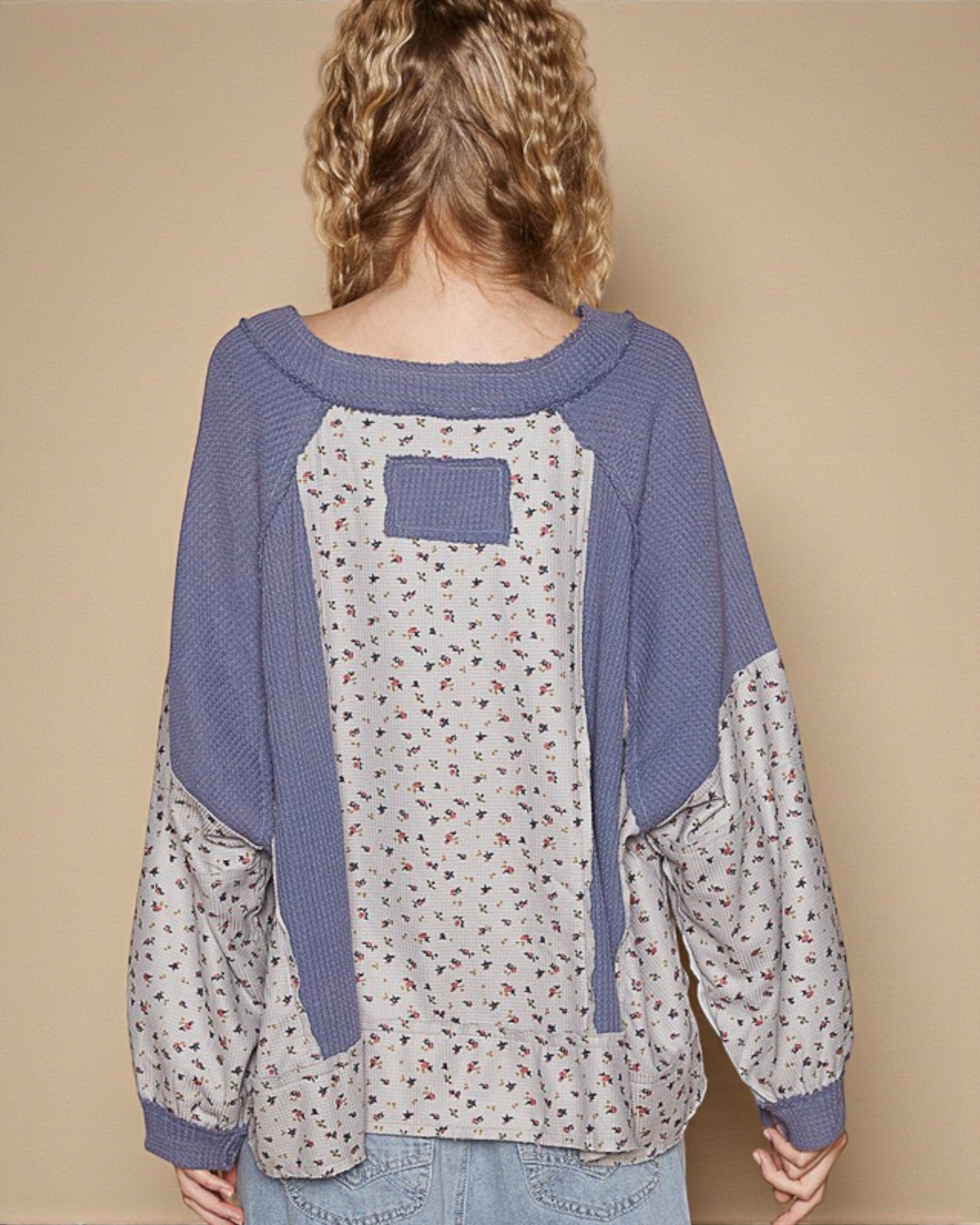 Person wearing a blue and patterned long-sleeve shirt against a beige background