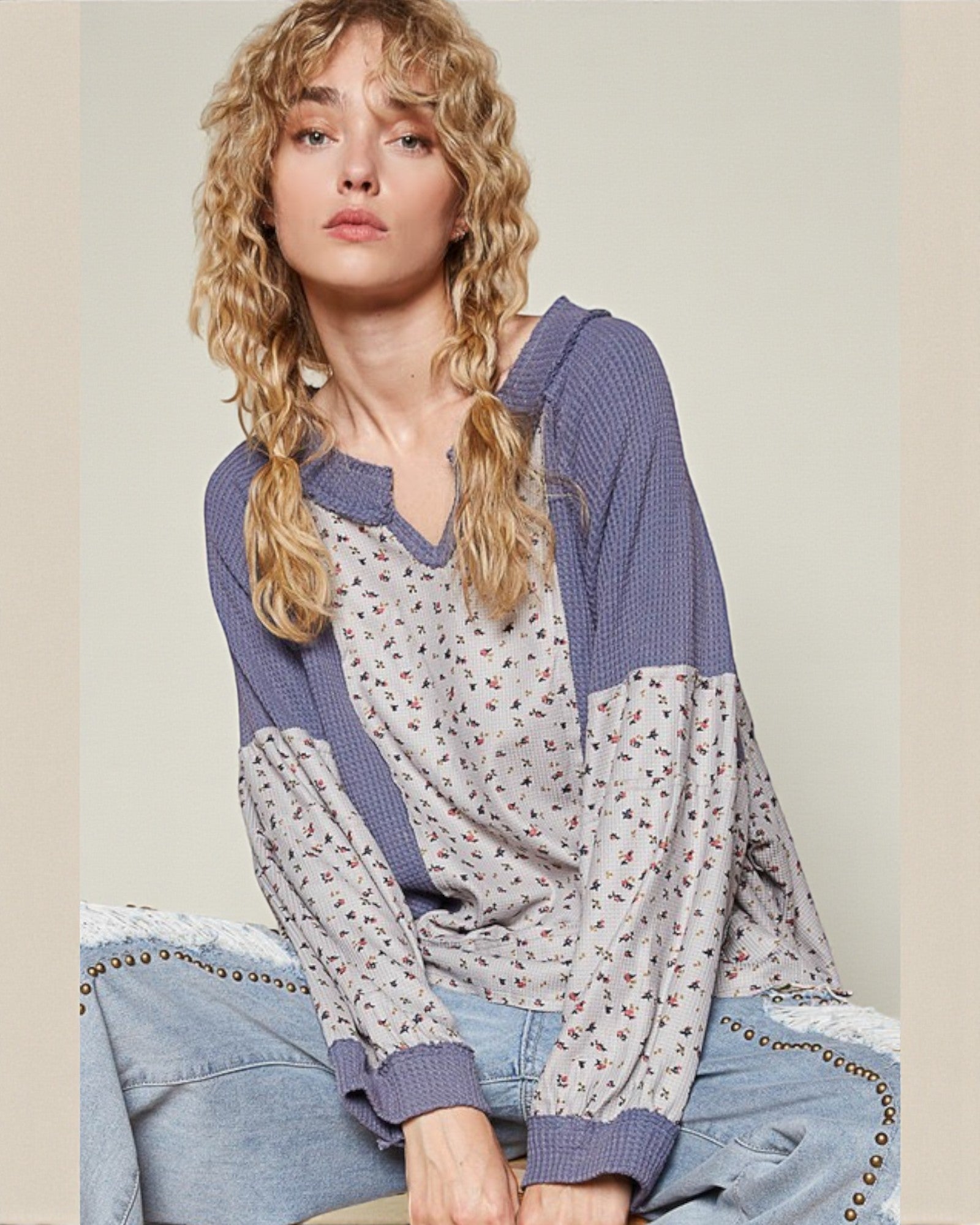 Woman wearing a floral top with purple sleeves and denim pants against a plain background