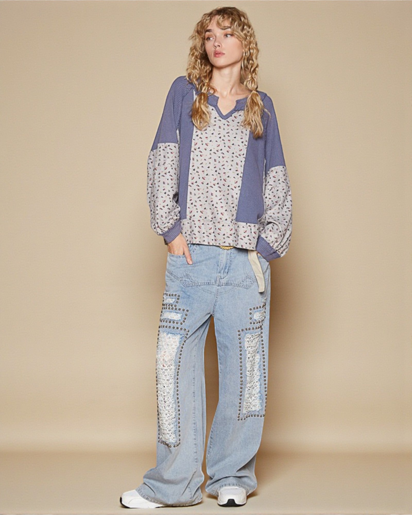 Woman wearing a patterned top and blue jeans on a beige background