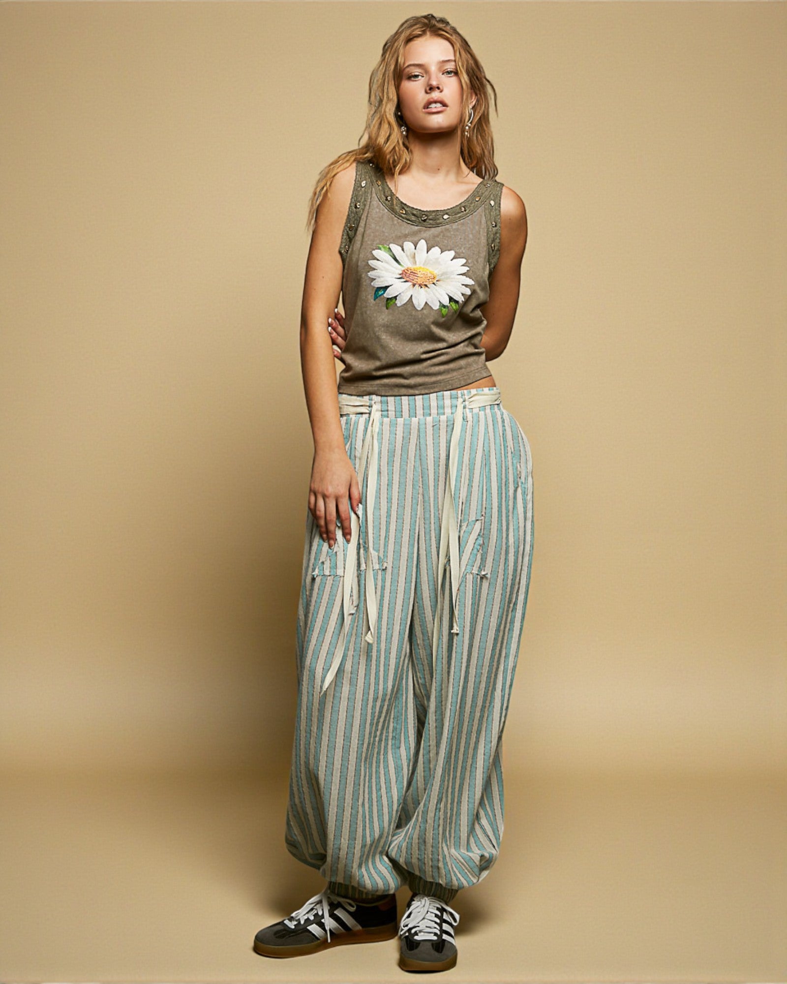 Woman wearing a tank top with a floral design and striped pants on a beige background