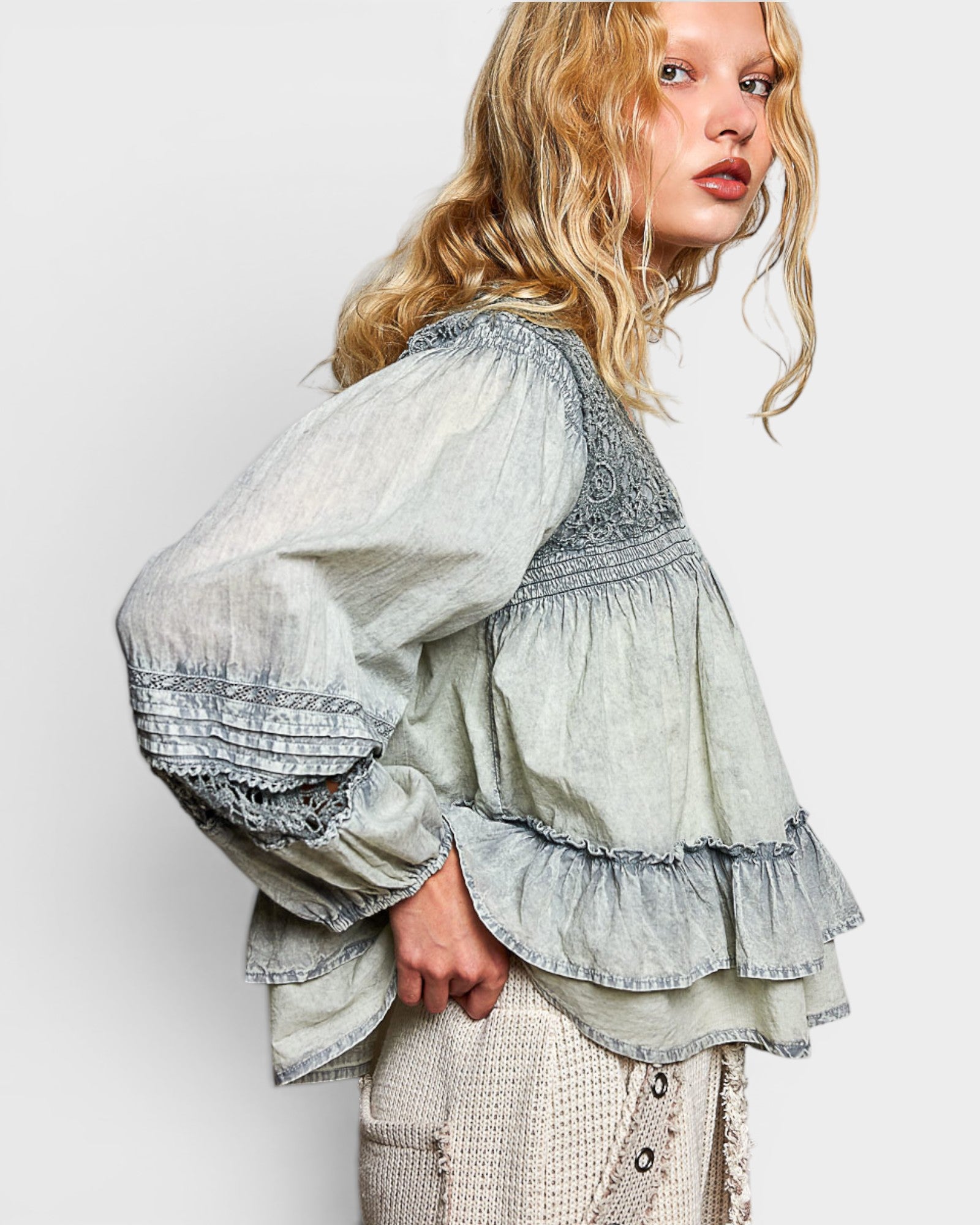 Woman wearing a layered blouse with intricate details on a plain background