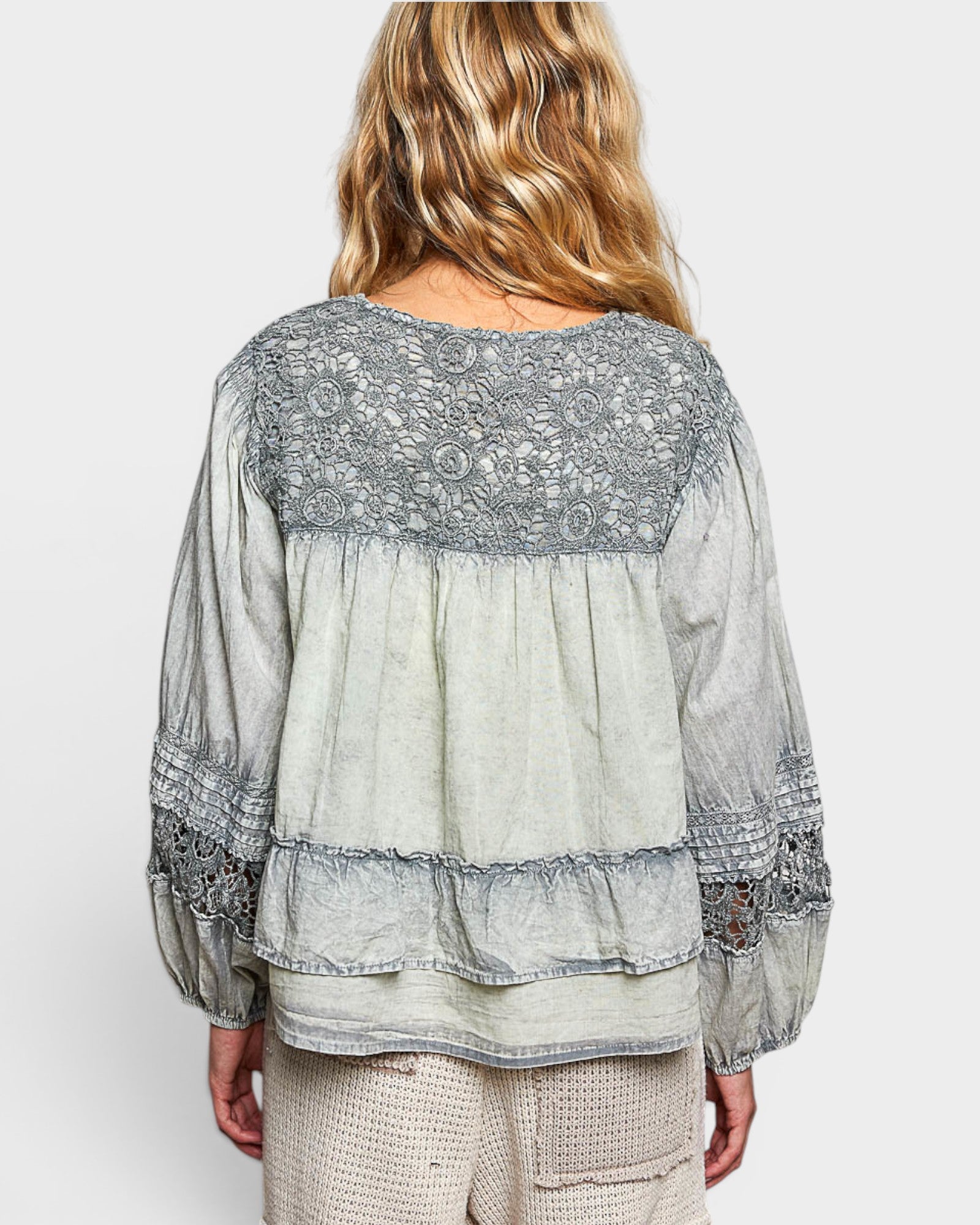 Woman wearing a light gray blouse with lace details on a white background