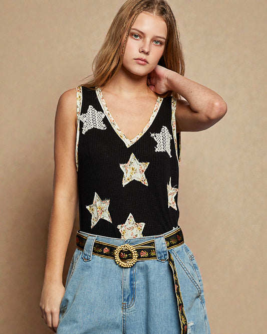 Woman wearing a black sleeveless top with star patterns and blue jeans against a beige background
