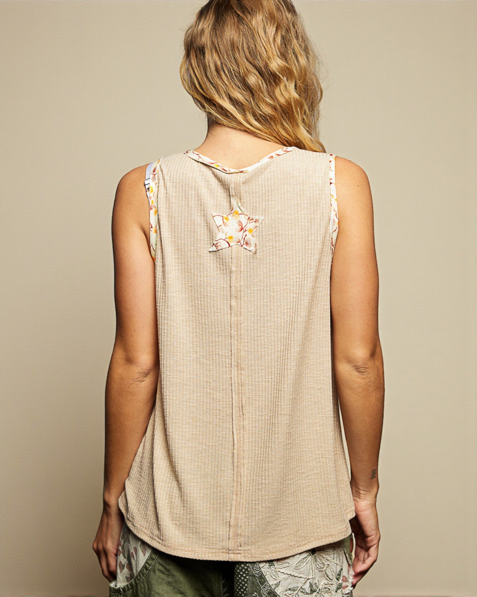 Person wearing a beige sleeveless top with floral embroidery on a neutral background