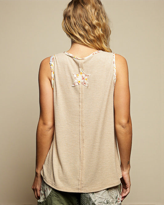 Person wearing a beige sleeveless top with floral embroidery on a neutral background