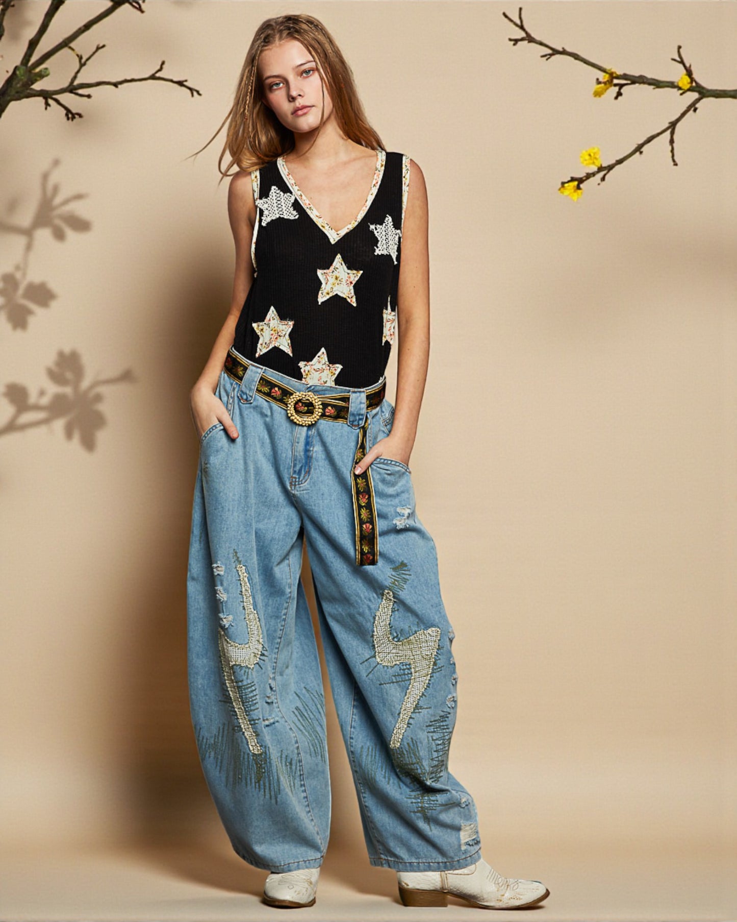 Woman wearing a black star-patterned top and blue jeans with decorative elements on a beige background