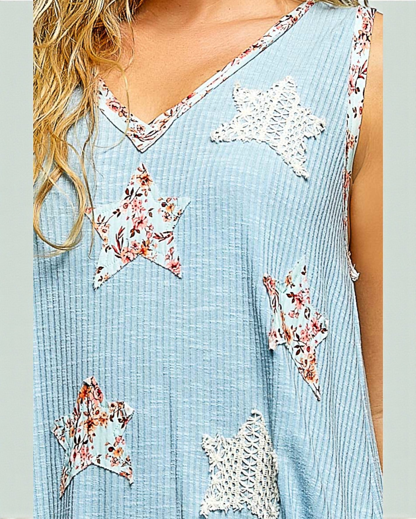 Light blue sleeveless top with star-shaped floral patches worn by a person.