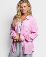 Woman wearing a pink shirt over a white lace top on a light gray background