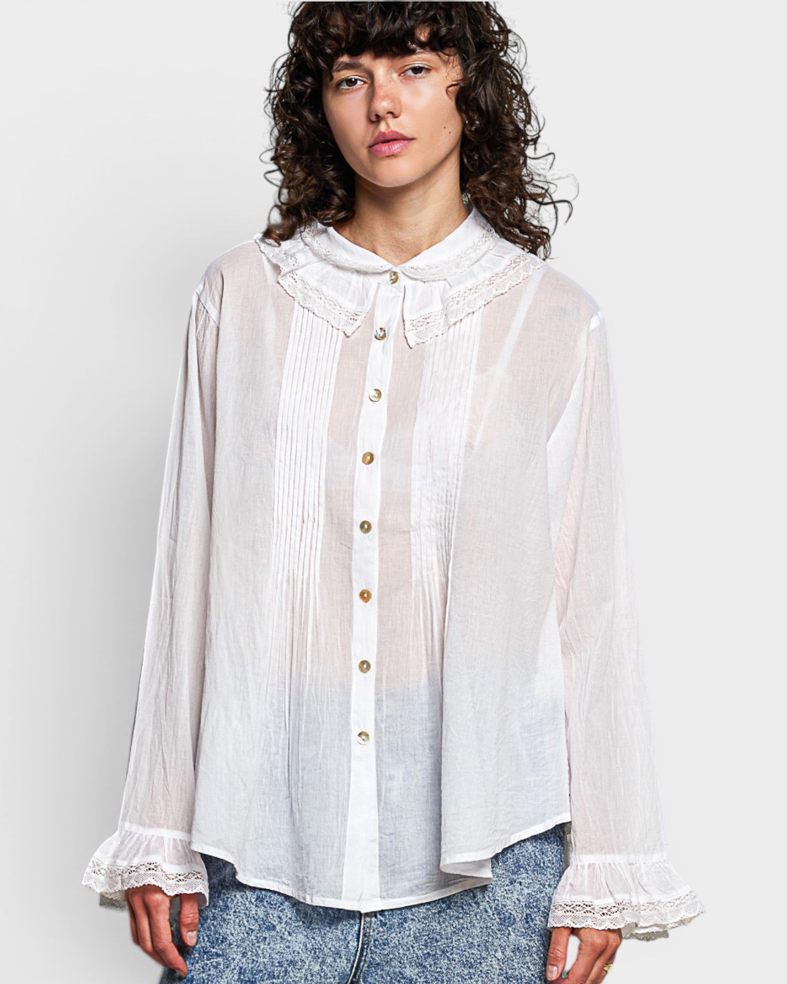 Woman wearing a white blouse with ruffled details on a plain background