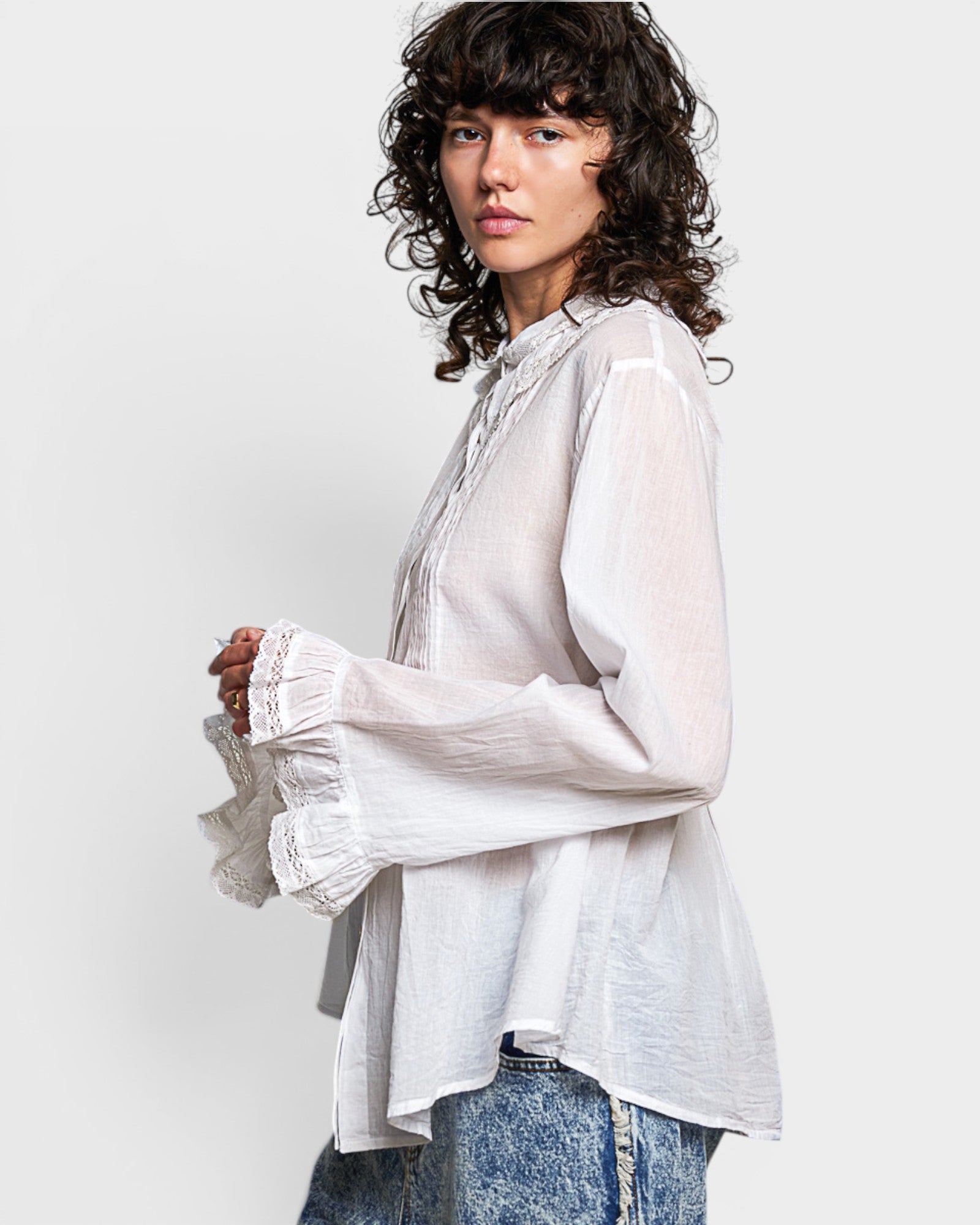 Woman wearing a light-colored blouse with lace details on a white background