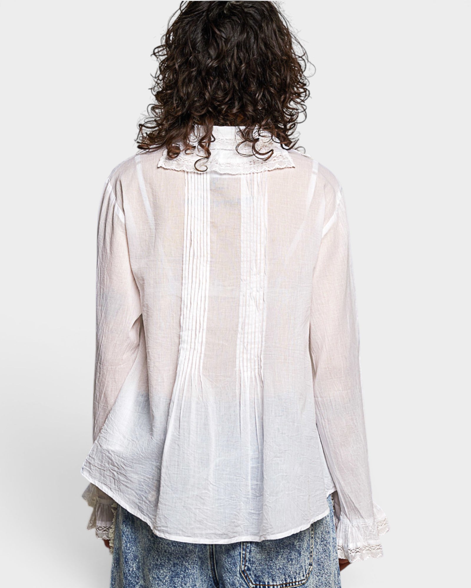 Person wearing a sheer white blouse with pleated details on a plain background