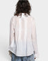 Person wearing a sheer white blouse with pleated details on a plain background