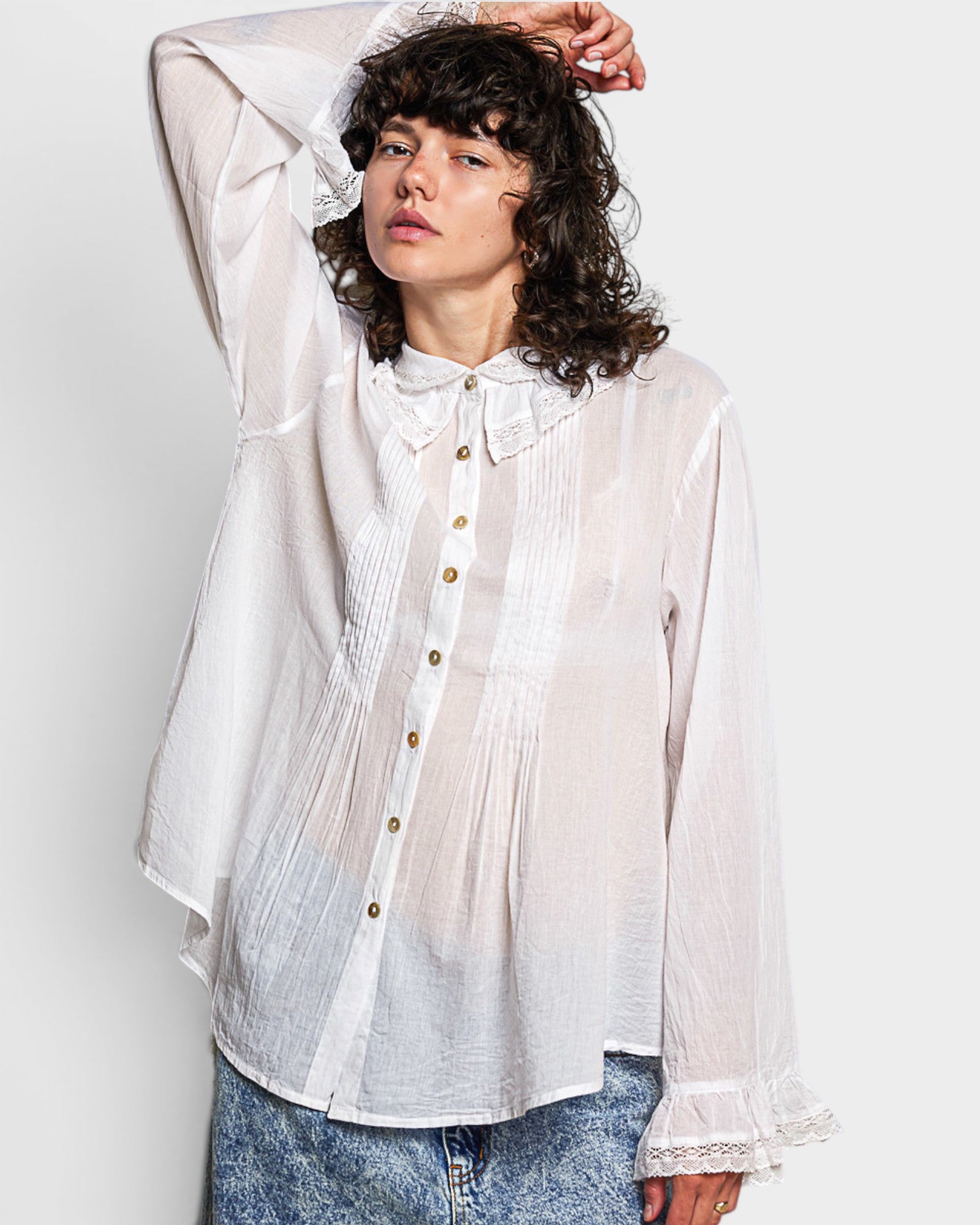 Woman wearing a white sheer blouse with lace details on a plain background