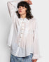 Woman wearing a white sheer blouse with lace details on a plain background