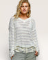 Woman wearing a textured white sweater over a floral top with gray pants on a plain background