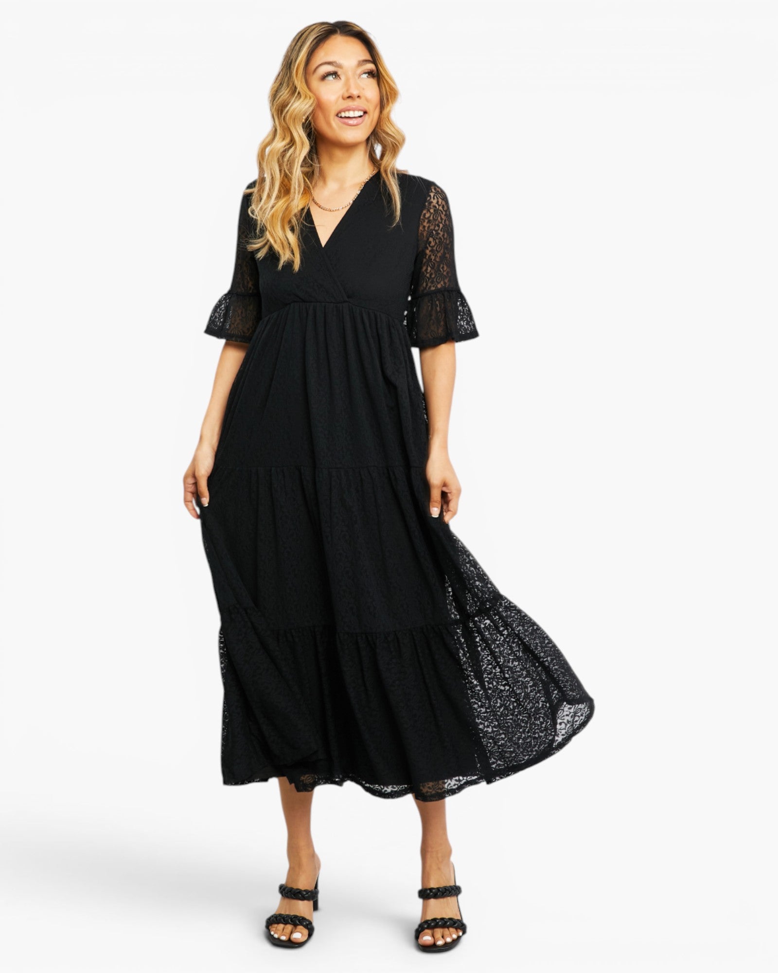 A woman modeling a black midi dress with a tiered skirt, lace short sleeves, and a V-neckline against a plain white studio background.