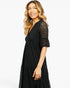 A woman wearing a black midi dress with lace flutter sleeves and a V-neckline, photographed against a clean white studio background.