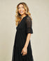 Woman wearing a black dress with lace sleeves against a beige background