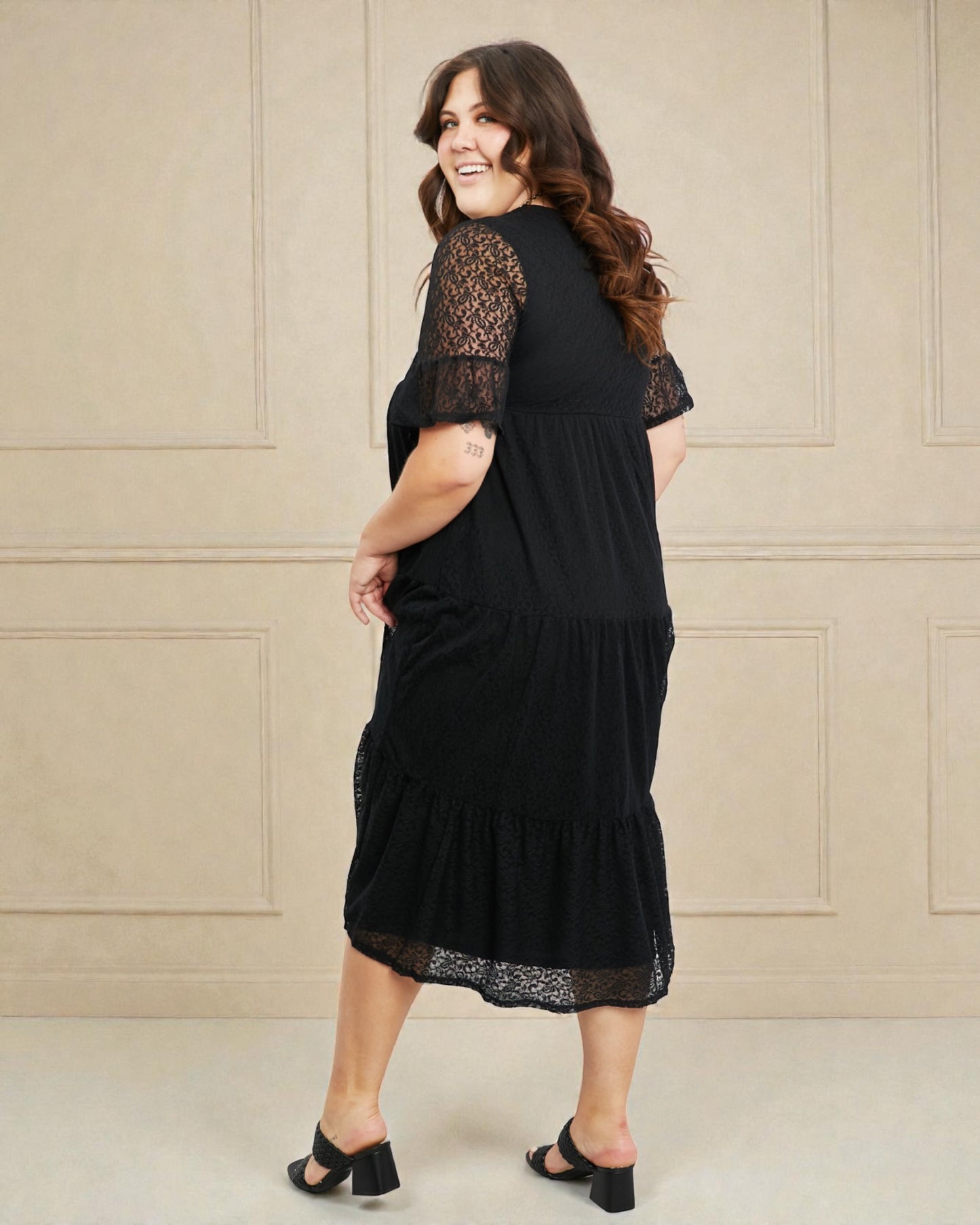 Woman wearing a black dress with lace details against a beige wall.