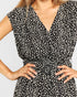 A close-up of a woman wearing a black wrap-style dress with an all-over white abstract print, featuring a V-neckline, cap sleeves, and a matching black belt with a square buckle.