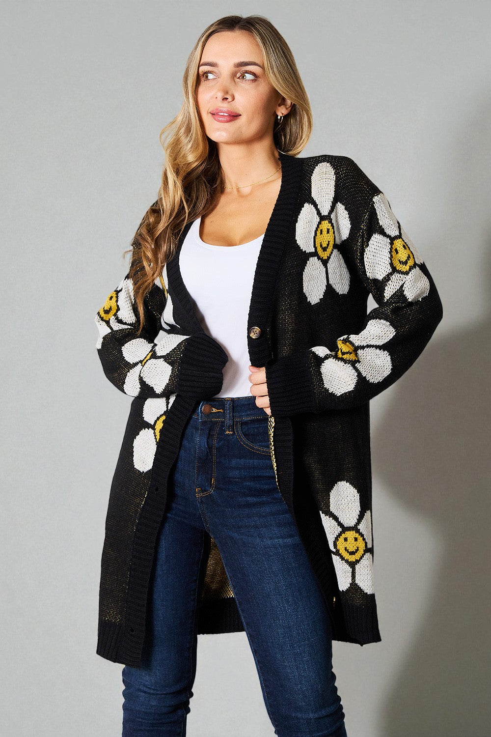 Woman wearing a black cardigan with white floral patterns and yellow centers on a gray background