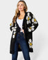 Woman wearing a black cardigan with white floral patterns on a plain background