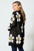 Woman wearing a black cardigan with white floral patterns on a white background