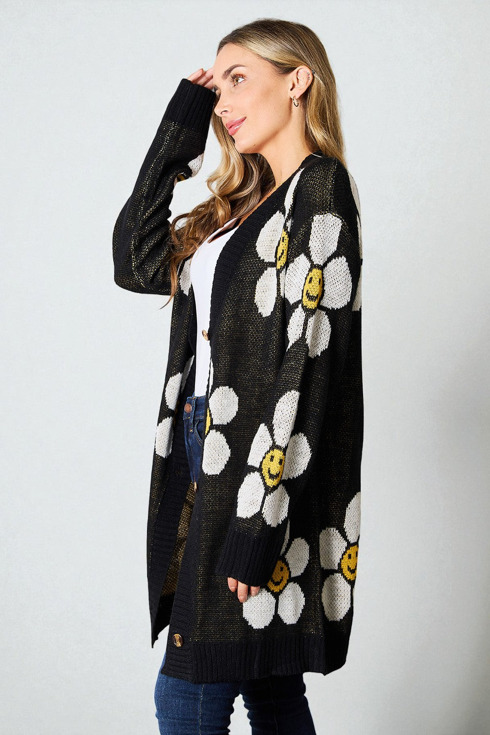 Woman wearing a black cardigan with white floral patterns and yellow centers on a plain background