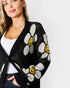 Woman wearing a black cardigan with white floral patterns and yellow centers on a white background