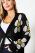Woman wearing a black cardigan with white floral patterns and yellow centers.