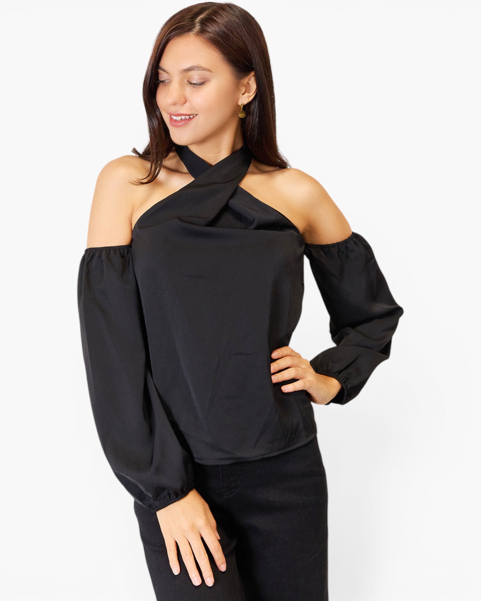 A woman modeling a black cold-shoulder top with a twisted halter-style neckline and long balloon sleeves, paired with black pants against a plain light gray studio background.