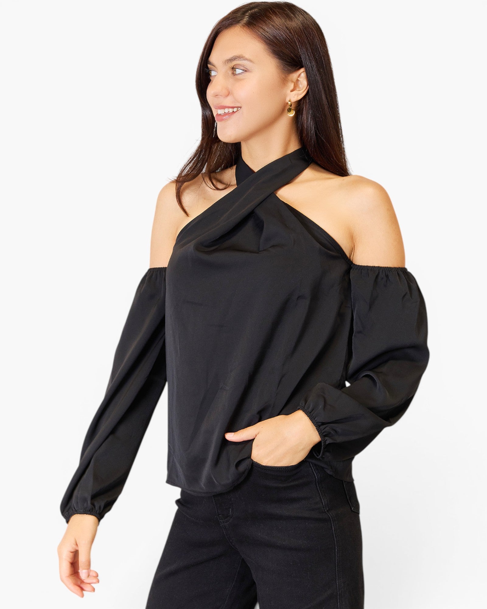 A woman wearing a black cold-shoulder long-sleeve blouse with a draped neckline and puffed sleeves, paired with black pants, against a light gray studio background.