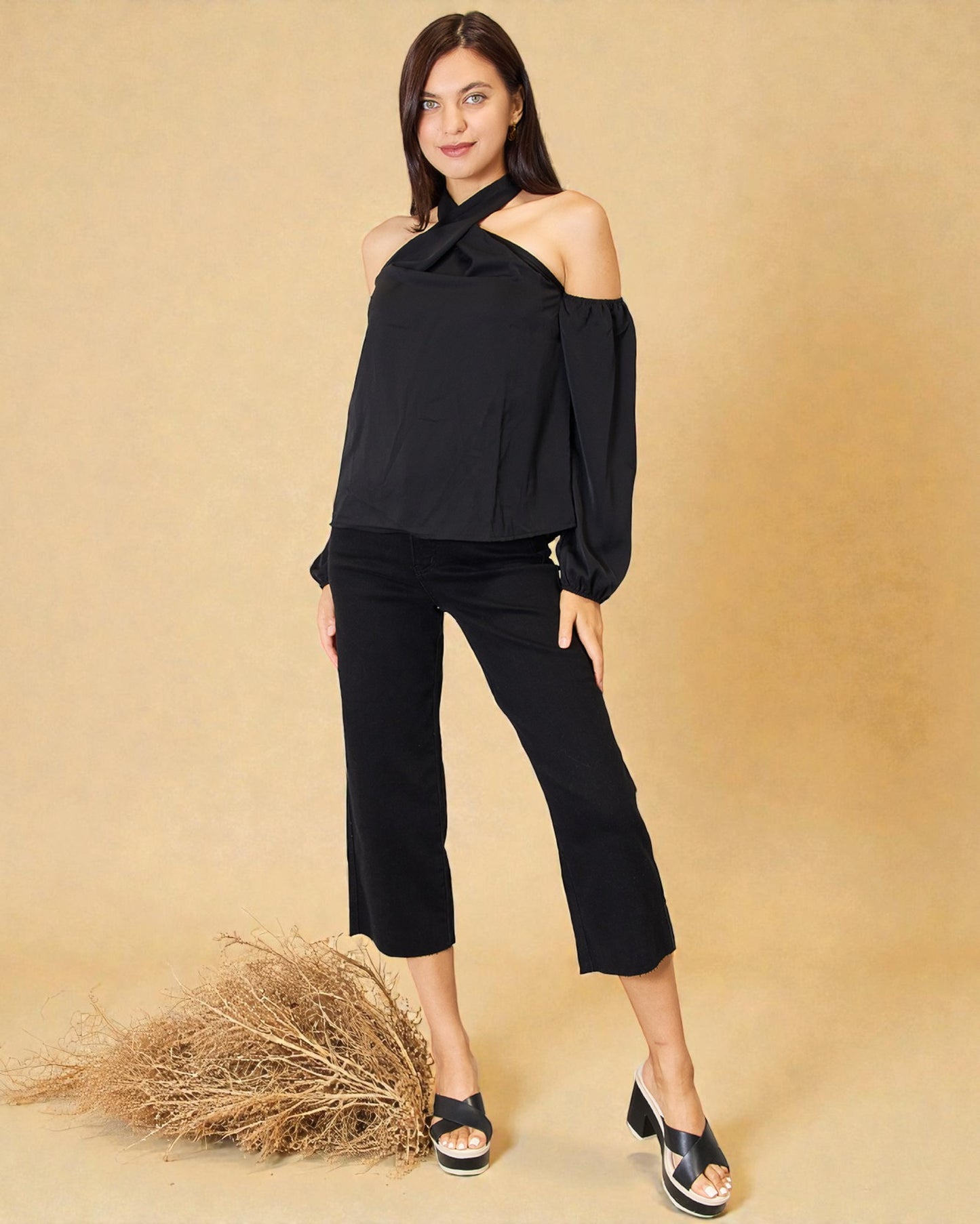 Woman wearing a black off-shoulder top and black pants against a beige background