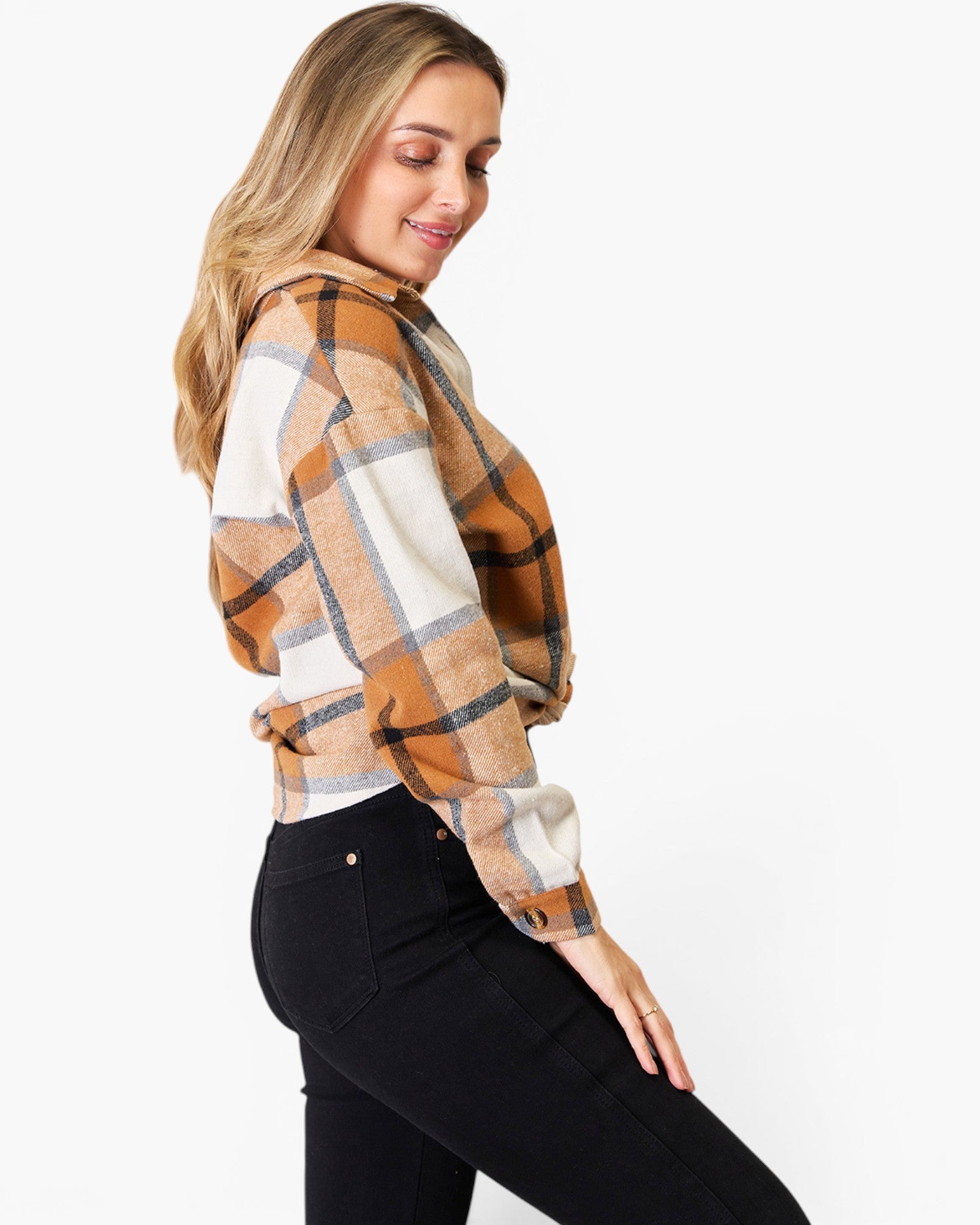 A woman wearing a long-sleeve plaid button-up shirt in brown, beige, and white, paired with black jeans, photographed against a solid white background.