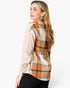 A woman wearing a long-sleeve plaid shirt, shown from a side-back angle against a plain white studio background.