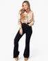 A woman modeling a beige and brown plaid button-up shirt with black flared jeans and tan slide sandals, photographed against a clean white studio background.