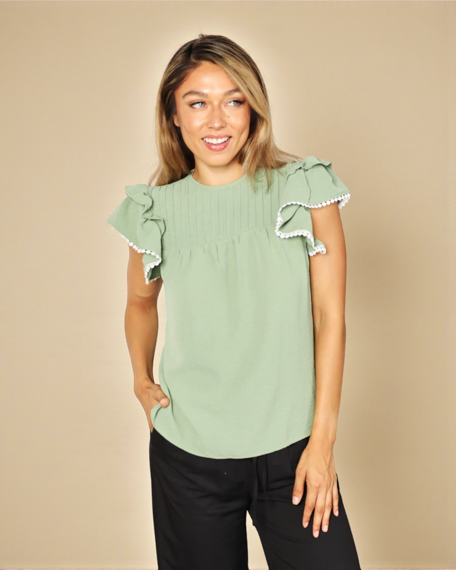 Woman wearing a light green blouse with ruffled sleeves against a beige background