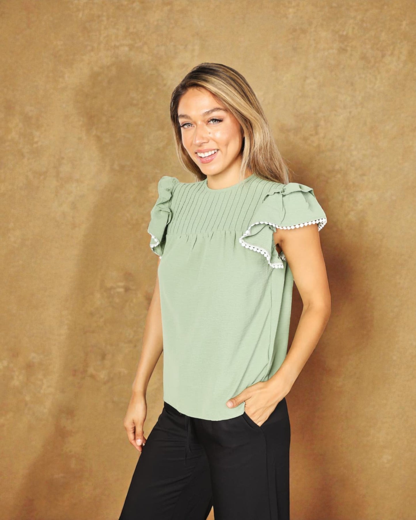 Woman wearing a green blouse with ruffled sleeves against a brown background