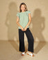 Woman wearing a green blouse with ruffled sleeves and black pants on a beige background