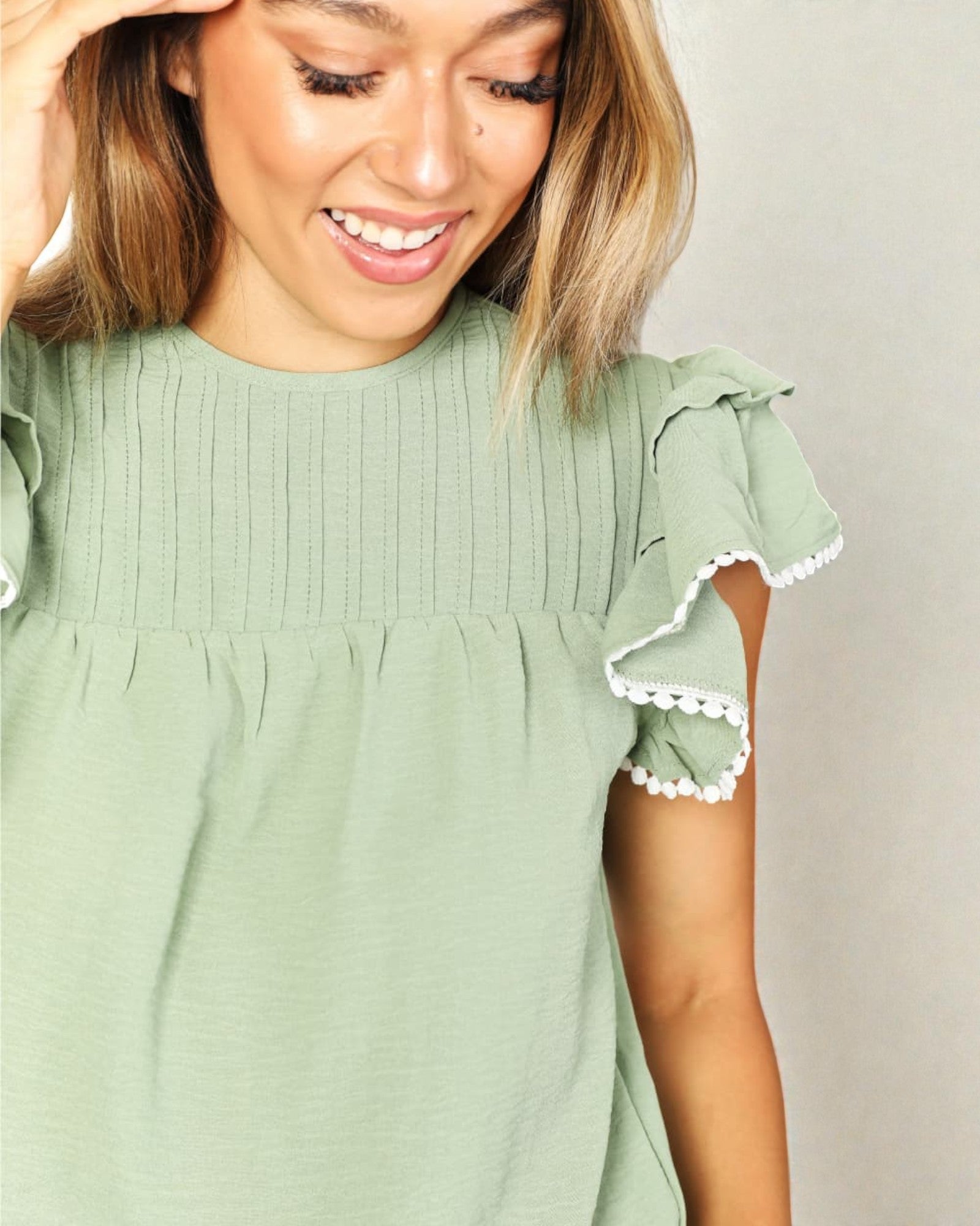 Woman wearing a green blouse with ruffled sleeves against a plain background