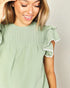 Woman wearing a green blouse with ruffled sleeves against a plain background