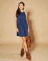 Woman wearing a blue dress with brown boots and a bag against a beige background