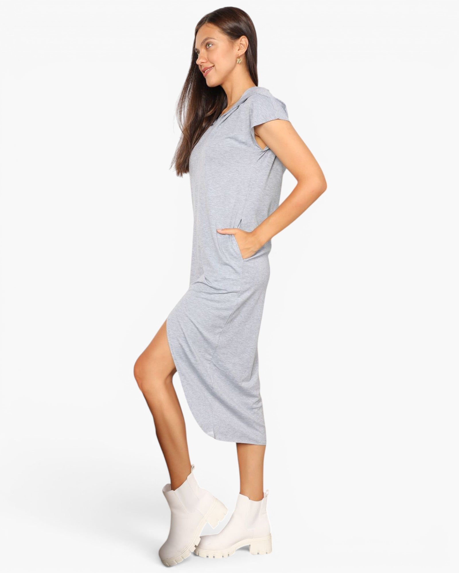 A woman modeling a light heather gray short-sleeve midi dress with side pockets, paired with white ankle boots, against a plain white studio background.