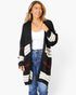 A woman modeling a black open-front cardigan with cream and red striped details, worn over a white tank top and blue jeans against a plain white background.
